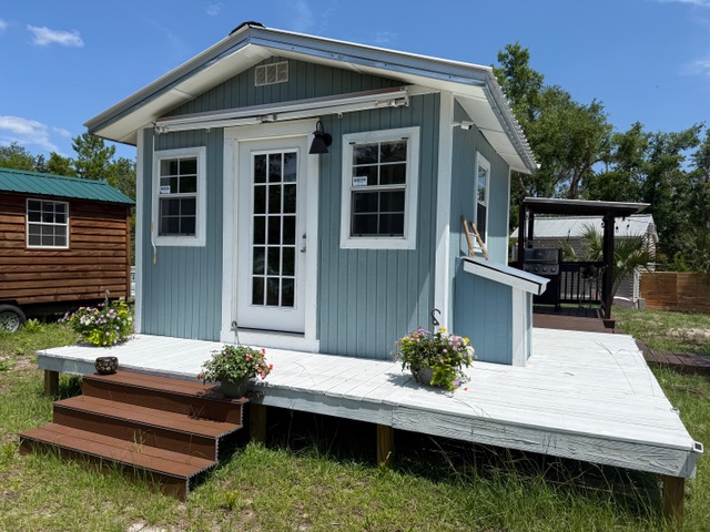 Small cottage with a white deck, steps, flower planters, and blue sky.