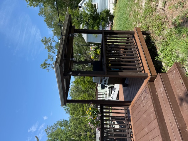 Outdoor deck with grill, seating, flowers, and surrounding trees.