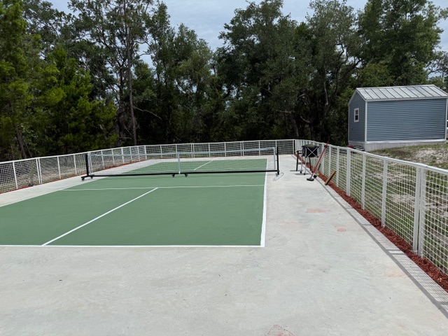 Outdoor pickleball court with white fencing, trees, and open playing space.